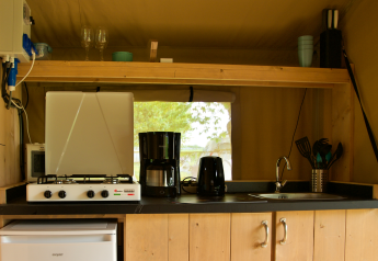 Coin cuisine d'une tente safari avec cuisinière, réfrigérateur, cafetière, évier et ustensiles.