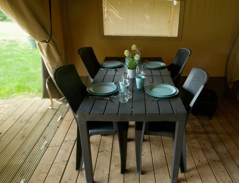 Table noire dressée pour quatre personnes avec chaises noires dans une tente safari sur plancher en bois.