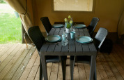 A black table set for four with black chairs inside a safari tent, featuring wood flooring and outdoor view.