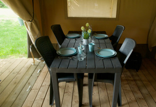 Zwarte tafel gedekt voor vier met zwarte stoelen in een safaritent met houten vloer en uitzicht naar buiten.