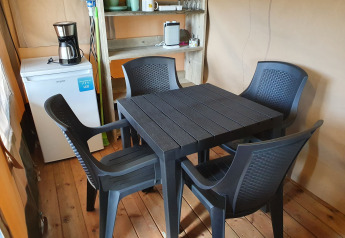 Interno di una tenda safari con tavolo in plastica nera, quattro sedie, frigo, macchina caffè e scaffale.