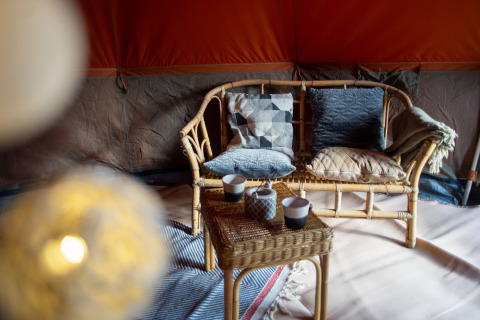 Intérieur d'une tente safari Bell avec un canapé en osier, coussins, plaid et tasses sur la table.