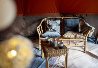 Cozy safari bell tent interior with wicker sofa, patterned pillows, throw blanket and mugs on table.