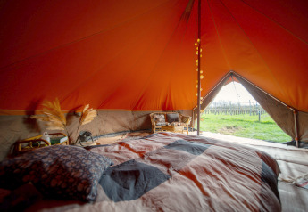 Interior view of a Bell tent safari tent with a cozy bed and a scenic view of fields through the doorway.