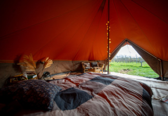 Binnenzicht van een Bell tent safari tent met bed en zicht op groene velden via de open tentdeur.