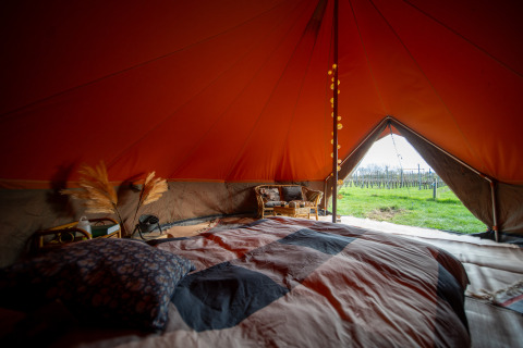 Vista interior de una tienda tipo Bell safari con cama acogedora y vistas a los campos por la entrada abierta.