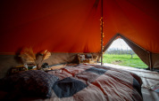 Vista interior de una tienda tipo Bell safari con cama acogedora y vistas a los campos por la entrada abierta.