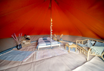 Interior of a Bell tent safari tent featuring a cozy bed, sofa, rugs and rustic decorative accents.