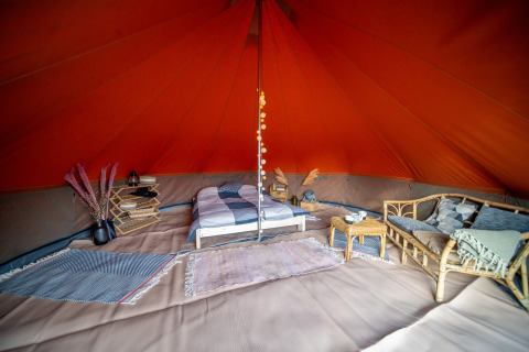 Interior de una tienda tipo Bell tent decorada con cama, sofá, alfombras y detalles rústicos.