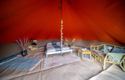 Interieur van een Bell tent safaritent ingericht met bed, zetel, tapijten en rustieke accenten.