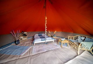 Interior de una tienda tipo Bell tent decorada con cama, sofá, alfombras y detalles rústicos.