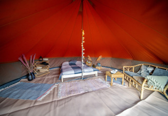 Interno di una tenda safari Bell tent con letto, divano, tappeti e tocchi decorativi rustici.