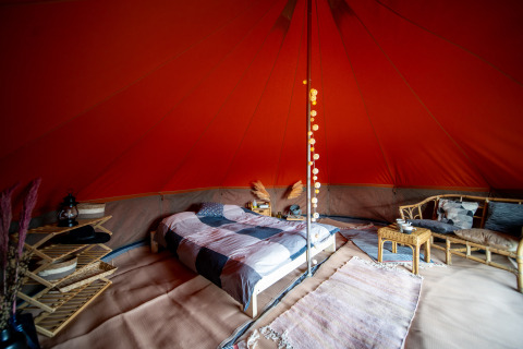 Interior de una tienda Bell de safari con cama cómoda, muebles de ratán y decoración acogedora.