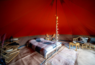 Interior de una tienda Bell de safari con cama cómoda, muebles de ratán y decoración acogedora.
