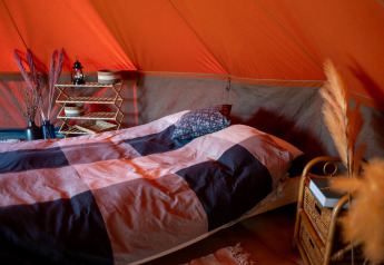Interior of the Bell tent safari tent showing a cozy bed with stylish decor and warm lighting accents.