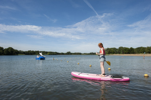 Chica de pie en paddleboard rosa en Camping Sevink Molen, Gelderland, Países Bajos, bajo cielo azul claro.