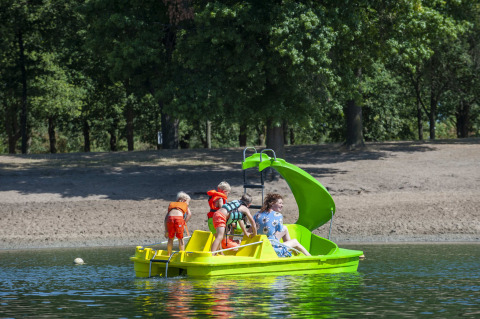 Niños y un adulto en un bote de pedales con tobogán en el lago de Camping Sevink Molen, Gelderland, Países Bajos.