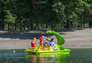 Niños y un adulto en un bote de pedales con tobogán en el lago de Camping Sevink Molen, Gelderland, Países Bajos.