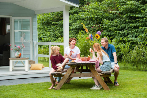 Familia disfruta de una comida al aire libre junto a una cabaña en Camping Sevink Molen, Gelderland, Países Bajos.