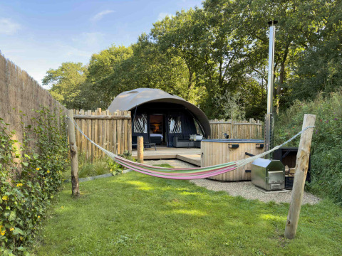 Cozy outdoor camping at Sevink Molen, Gelderland, with hammock, hot tub, and tent in a fenced setting.