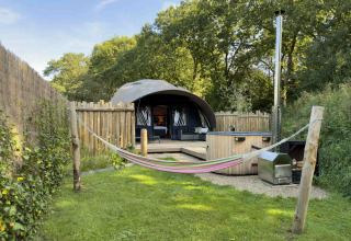 Gezellige kampeerplek bij Sevink Molen, Gelderland, met hangmat, hottub en tent in een omheinde tuin.