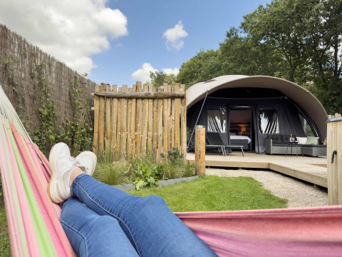 Persoon ontspant in een hangmat voor een luxetent bij Camping Sevink Molen, Gelderland, Nederland.