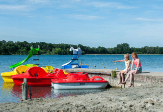 Due ragazze sedute vicino al lago con pedalò colorati al Camping Sevink Molen, Gelderland, Paesi Bassi.