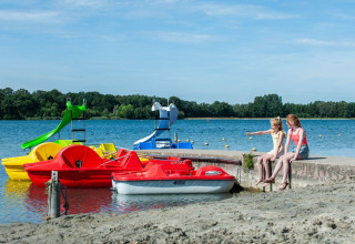 Due ragazze sedute vicino al lago con pedalò colorati al Camping Sevink Molen, Gelderland, Paesi Bassi.