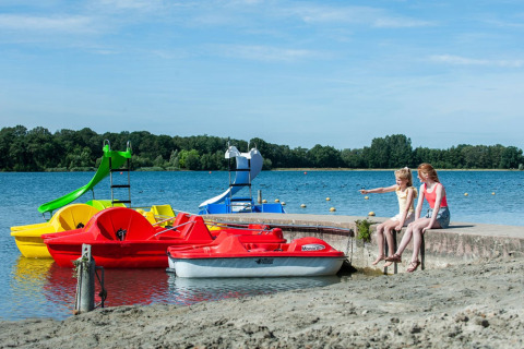 Due ragazze sedute vicino al lago con pedalò colorati al Camping Sevink Molen, Gelderland, Paesi Bassi.