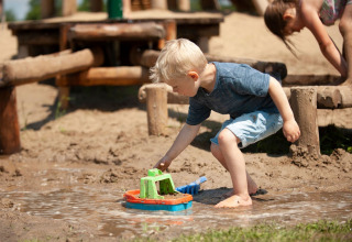 Junge spielt mit Spielzeugboot im Matsch auf dem Spielplatz im Camping Sevink Molen, Gelderland.