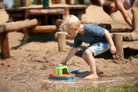 Niño jugando con un barco de juguete en el barro en un parque infantil de Camping Sevink Molen, Gelderland.