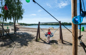 En pige sidder på en gynge ved stranden i Camping Sevink Molen, Gelderland, Holland, på en solrig dag.