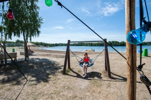 Fille assise sur une balançoire près du lac au Camping Sevink Molen, parc de vacances en Gueldre, Pays-Bas.