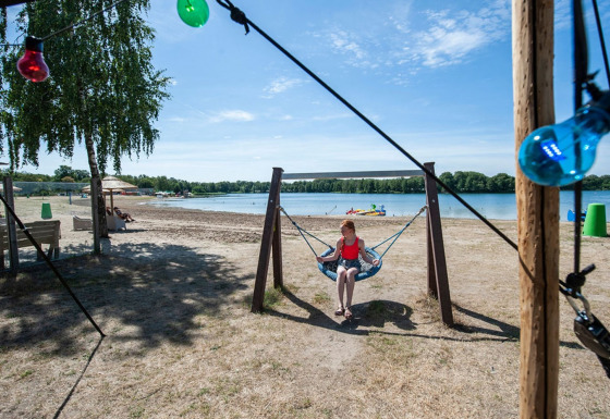 A girl sits on a swing by the lakeside at Camping Sevink Molen holiday park in Gelderland, Netherlands.