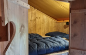 Acogedora habitación de madera con cama y edredón azul en tienda Safari con sanitario en Camping le Roc, Francia.