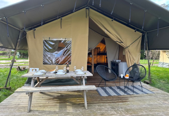 Safari tent with open entrance, wooden picnic table set for dining, and modern chairs on outdoor deck.