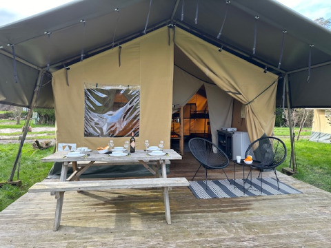 Safari tent with open entrance, wooden picnic table set for dining, and modern chairs on outdoor deck.