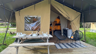 Safari tent with open entrance, wooden picnic table set for dining, and modern chairs on outdoor deck.