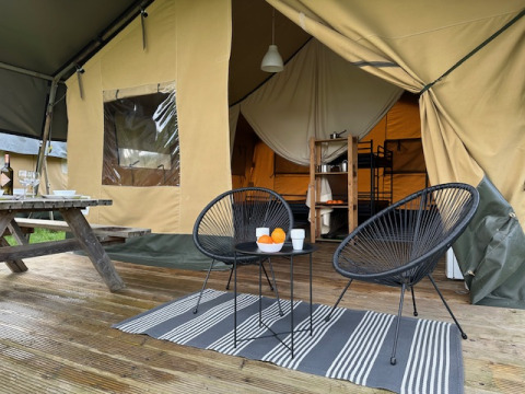 Tienda safari en Camping De La Vallée en Bélgica con terraza de madera, sillas modernas y ambiente acogedor.