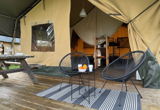Safari tent at Camping De La Vallée in Belgium featuring a wooden deck, modern chairs, and a cozy interior view.
