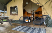 Tienda safari en Camping De La Vallée en Bélgica con terraza de madera, sillas modernas y ambiente acogedor.