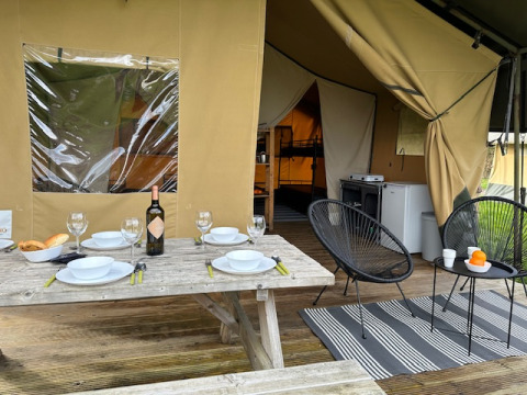 Zona de comedor al aire libre en tienda safari de Camping De La Vallée en Bélgica, mesa puesta y sillas.
