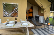 Zona de comedor al aire libre en tienda safari de Camping De La Vallée en Bélgica, mesa puesta y sillas.
