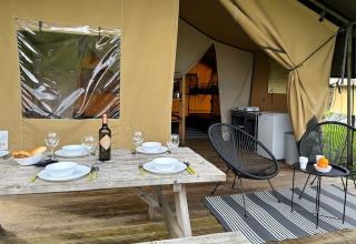 Area pranzo esterna al safari tent presso Camping De La Vallée in Belgio, tavolo apparecchiato e sedie.