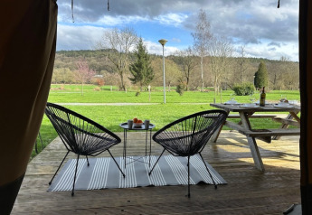 Vista da una tenda safari al Camping De La Vallée, Belgio, con area salotto esterna e paesaggio verde.
