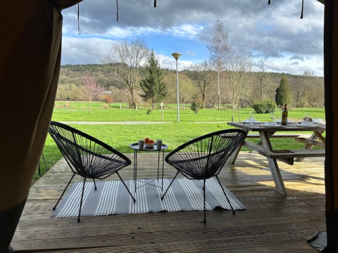Blick aus einem Safarizelt auf Camping De La Vallée, Belgien, mit Sitzbereich und grüner Landschaft.
