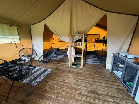 Interior de una tienda safari en Camping De La Vallée, Bélgica, con sala, cocina y literas visibles.