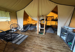Interior de una tienda safari en Camping De La Vallée, Bélgica, con sala, cocina y literas visibles.