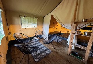 Vista interior de una tienda safari en Camping De La Vallée, Bélgica, con sillas, mesa y estantería de cocina.