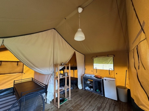 Interior de una tienda safari en Camping De La Vallée, Bélgica, con cama, cocina y área de descanso.